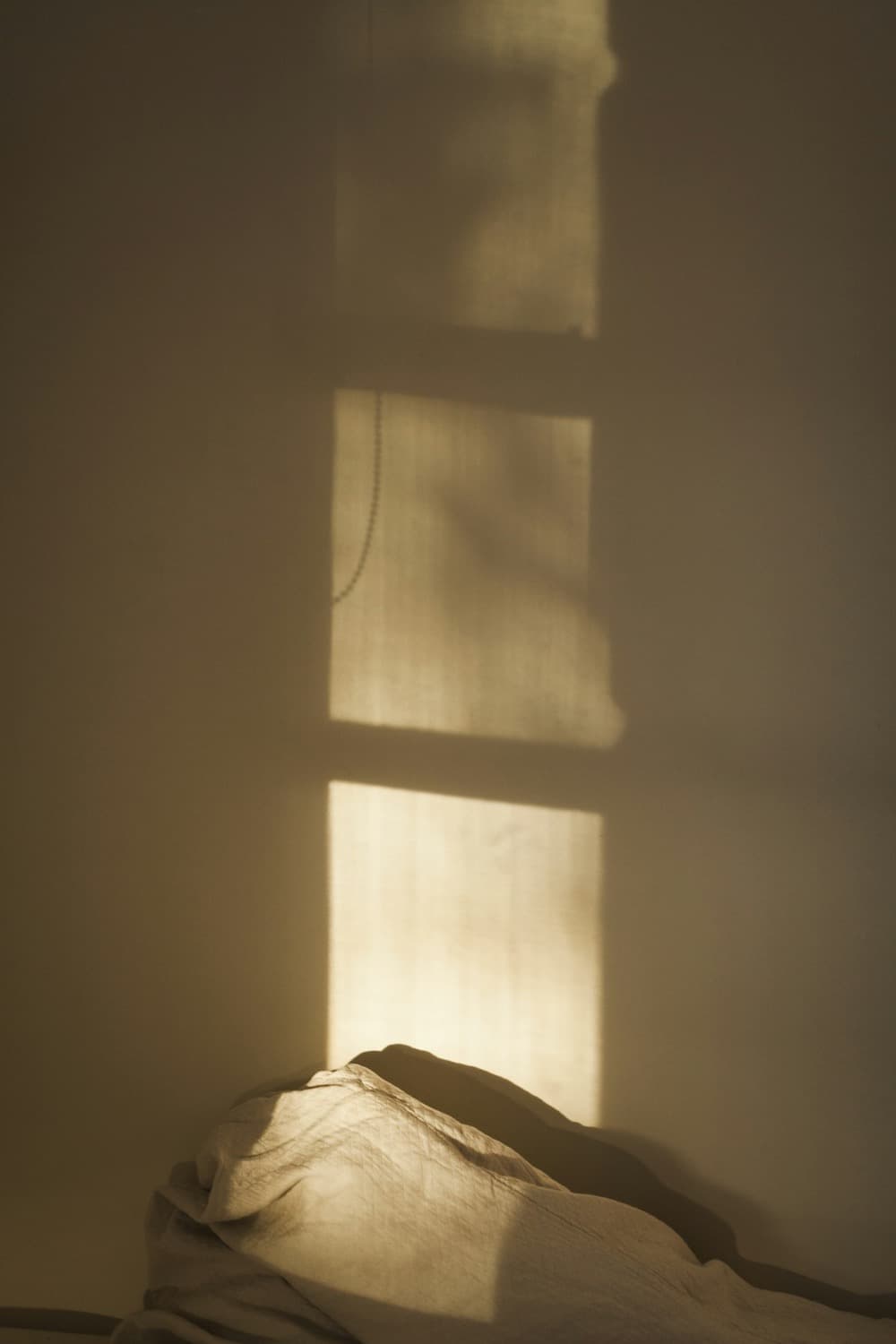 A sombra de uma janela desenhada na parede de um quarto, com a luz do começo do dia.